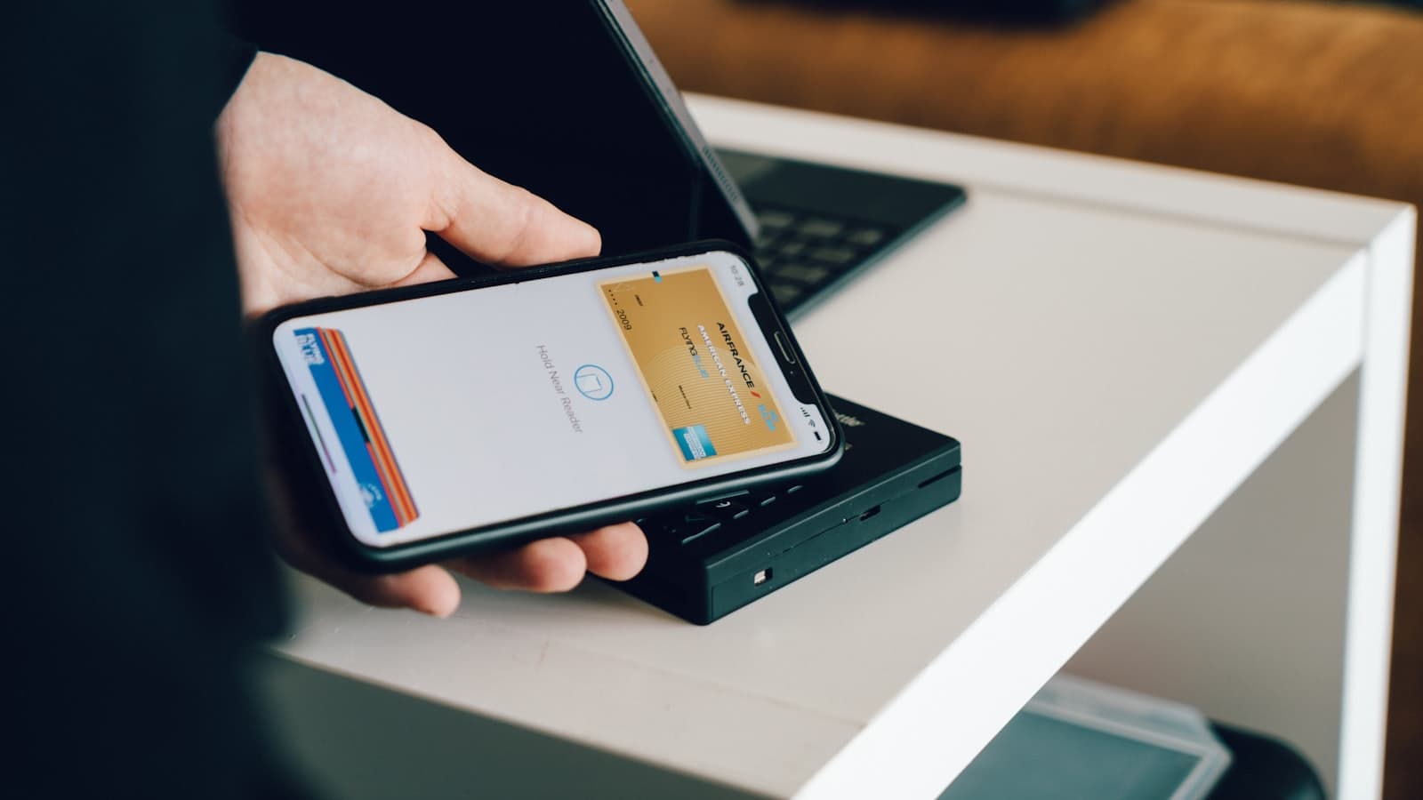 Persona pagando con el celular apoyado sobre una terminal de cobro